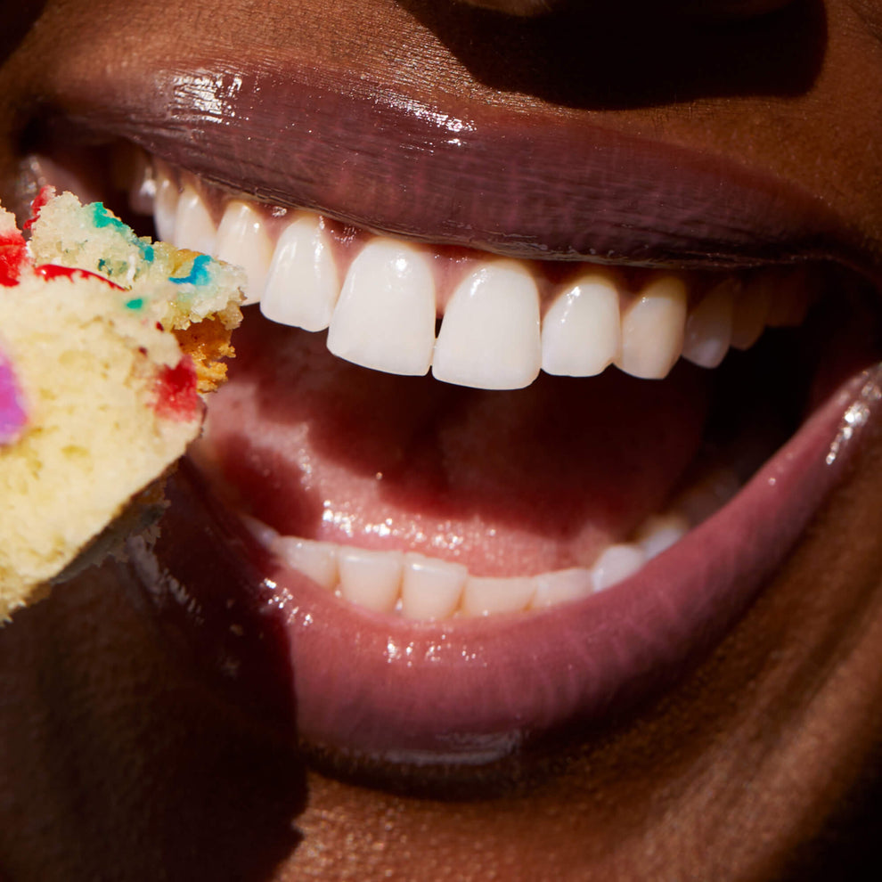 [A close up of a model wearing Tower 28 Beauty's LipSoftie™ Lip Treatment in Confetti Cake on her lips