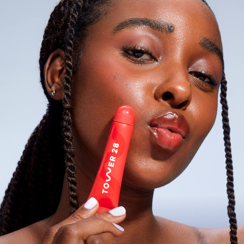 A close up of a model holding Tower 28 Beauty's LipSoftie™ Lip Treatment from the Set and wearing it on her lips