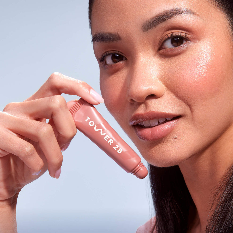 A close up of a model holding Tower 28 Beauty's LipSoftie™ Lip Treatment from the Set and wearing it on her lips