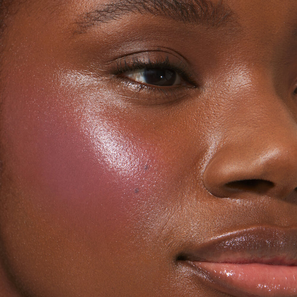 A close-up of a model with medium skin tone wearing Tower 28 Beauty's BeachPlease Cream Blush in Party Hour