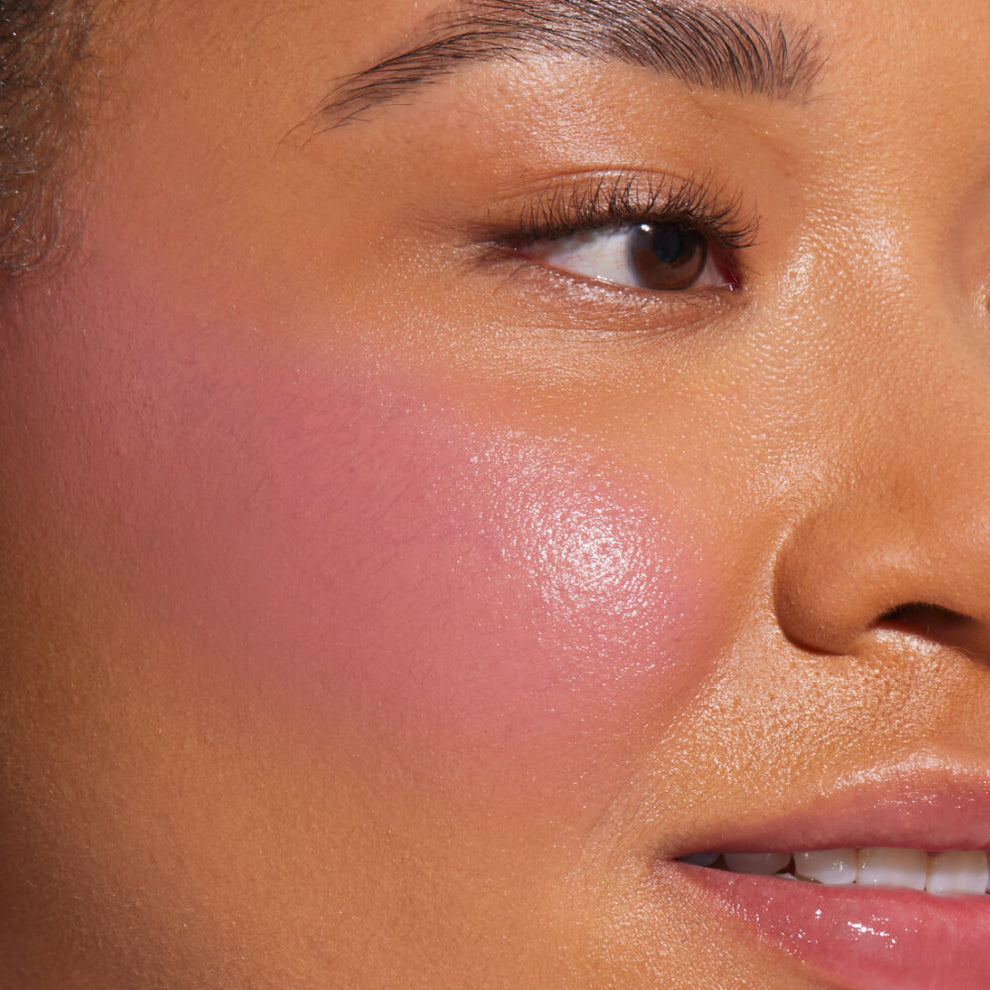 A close-up of a model with medium skin tone wearing Tower 28 Beauty's BeachPlease Cream Blush in Party Hour