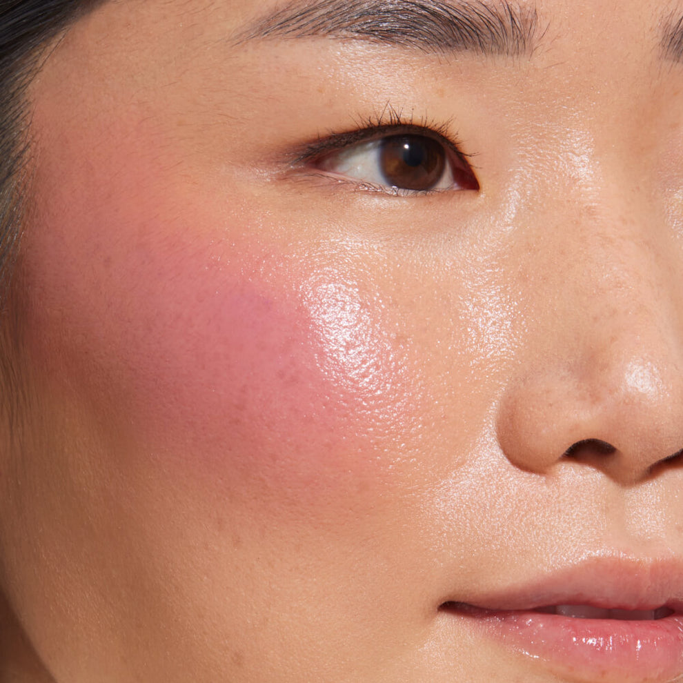 A close-up of a model with medium skin tone wearing Tower 28 Beauty's BeachPlease Cream Blush in Party Hour