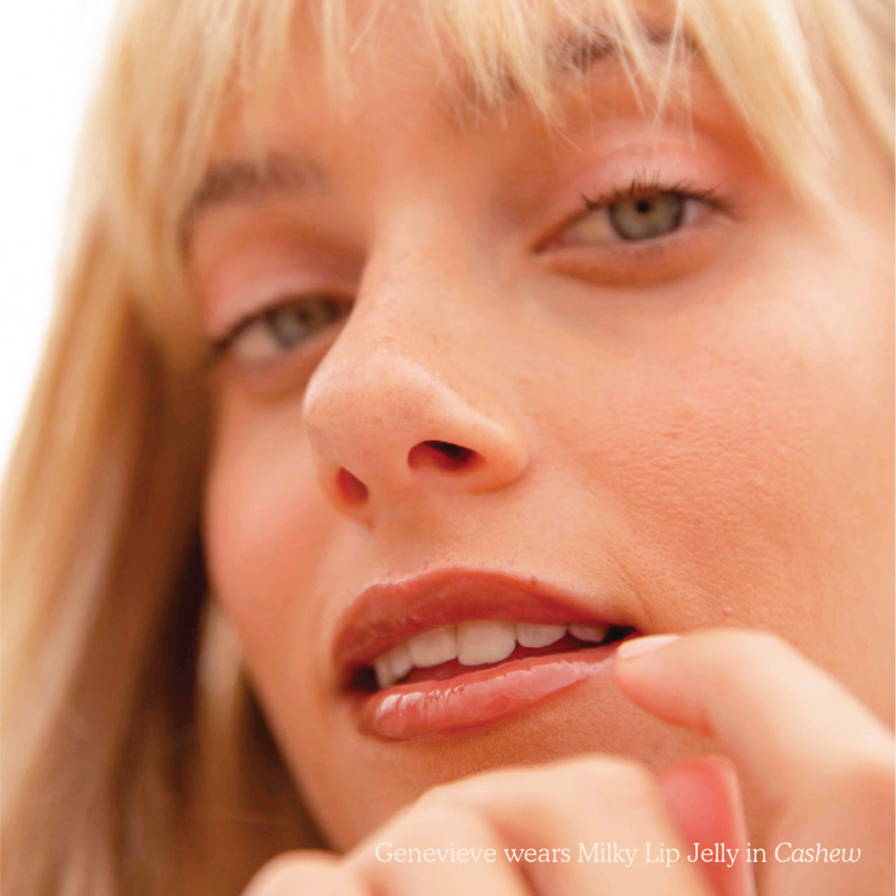 Closeup photo of a girl smiling with very glossy lips, wearing the Tower 28 Beauty ShineOn Milky Lip Jelly shade in Cashew (a milky rosy-brown)