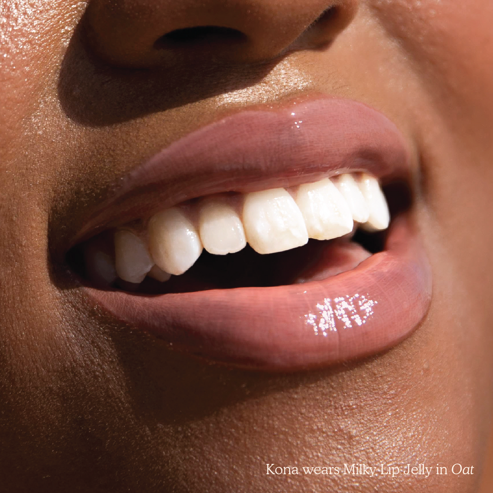 Closeup photo of very glossy lips, smiling and wearing the Tower 28 Beauty ShineOn Milky Lip Jelly shade in Oat (a milky peachy-pink)